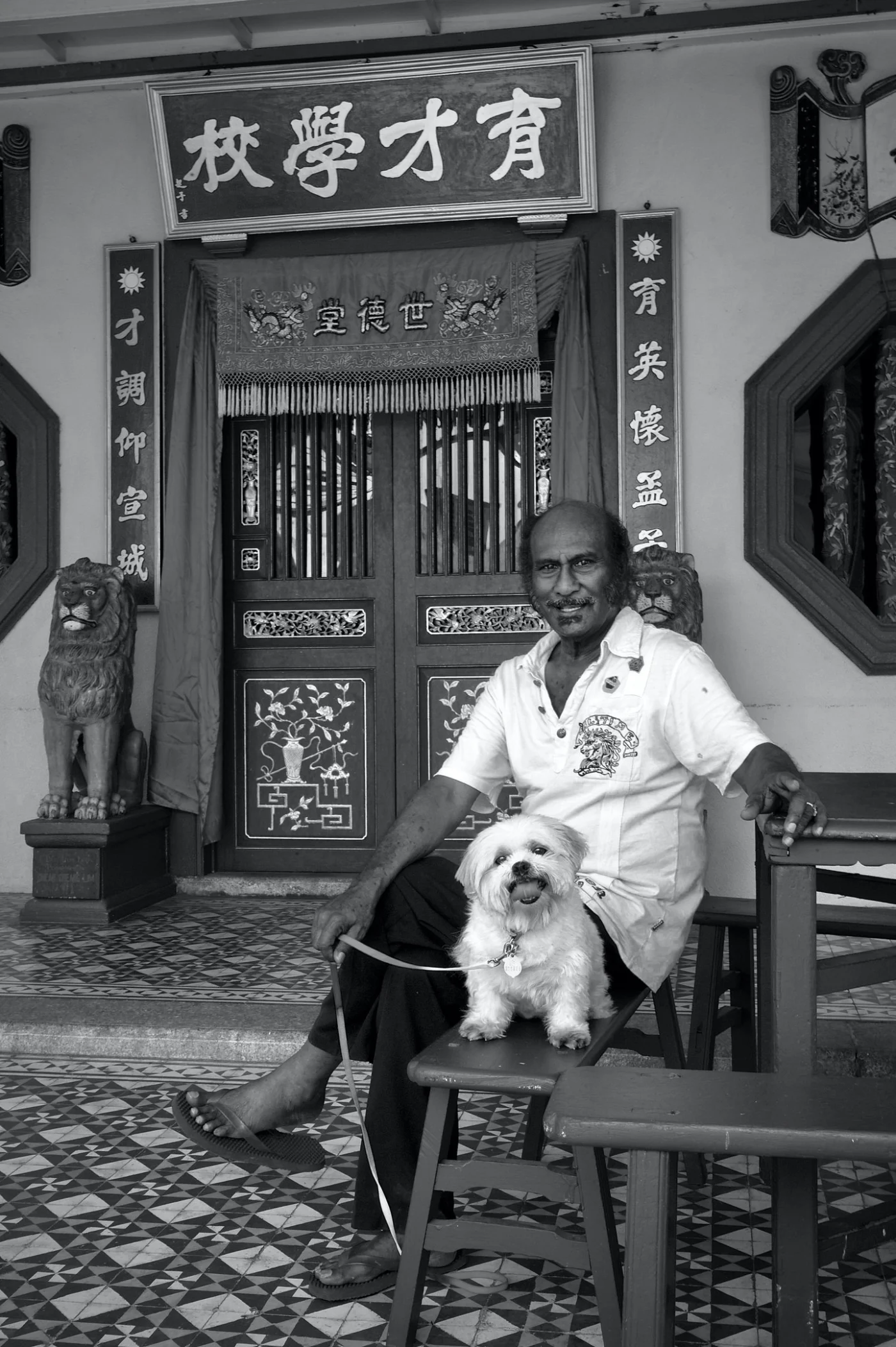 An Indian man and his dog sit outside a temple in Penang by photographer Peter Pickering